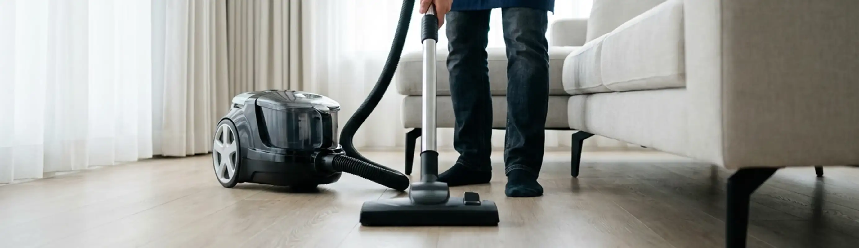 Professional house cleaner vacuuming a living room floor with a canister vacuum cleaner, Evansville, IN.