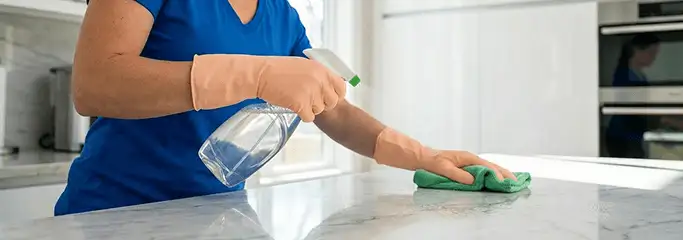 Maid service worker spraying and wiping a kitchen countertop with a microfiber cloth for sanitizing, Evansville, IN.