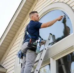 Professional window cleaner on a ladder using a squeegee to clean an exterior arched window, Evansville, IN.