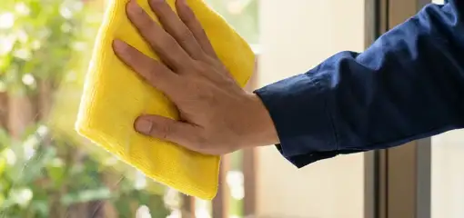 House cleaner wiping a glass window with a yellow microfiber cloth for streak-free cleaning, Evansville, IN.